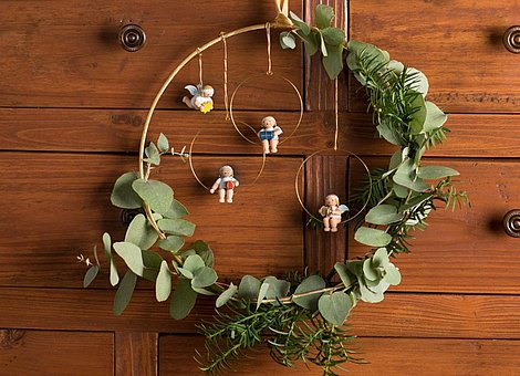 [Translate to Englisch (US):] Weihnachtskranz mit handgefertigten Margeritenengeln an braunem Schrank